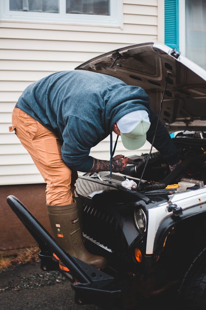 Male master in work clothes standing near car trunk during repair service near wall of house